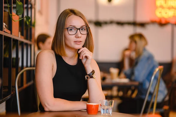 Hermosa mujer atractiva en gafas negras. Feliz chica de negocios trabajando en un café, sentada a la mesa —  Fotos de Stock