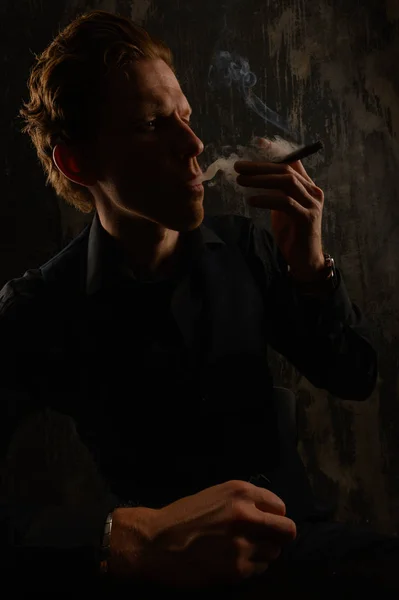 Jistý příležitostný mladý muž a kouřící cigaretu. Studiový portrét na tmavém pozadí. — Stock fotografie