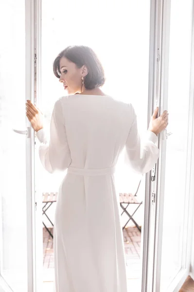 Chica en vestido blanco abre la puerta al balcón. día de la boda — Foto de Stock
