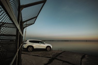 Gün batımında plaja yakın deniz kenarında beton yolda park edilmiş spor ve modern tasarıma sahip beyaz kompakt SUV araba