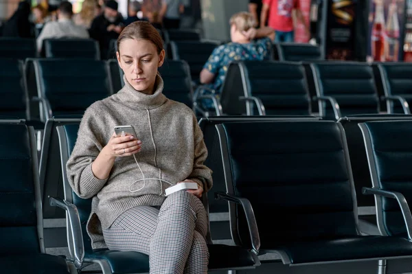 Młoda dziewczyna na lotnisku czeka na jej odejście. Przewijanie smartfonu — Zdjęcie stockowe