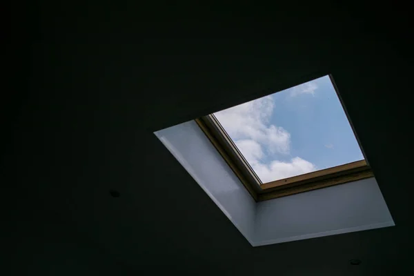 Patrząc w górę na błękitne zachmurzone niebo przez nowoczesne okno sufitu kwadratowego — Zdjęcie stockowe