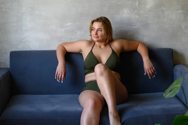 Krásná baculatá žena v béžových plavkách sedící na pohovce — Stock fotografie