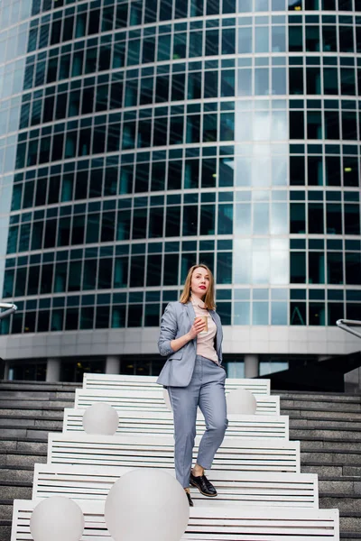 Seitenansicht einer reifen Frau im Business-Anzug, die nach Hause geht und telefoniert. Seniorin benutzt Handy auf Stadtstraße mit städtischem Hintergrund — Stockfoto