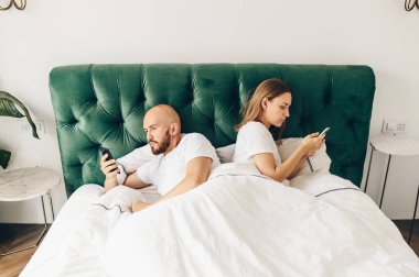Genç çift telefonlarıyla yatakta yatıyor. İletişim ve ilişki sorunları.