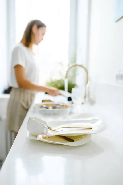 Bella giovane donna sorridente che lava i piatti nella moderna cucina bianca. — Foto Stock