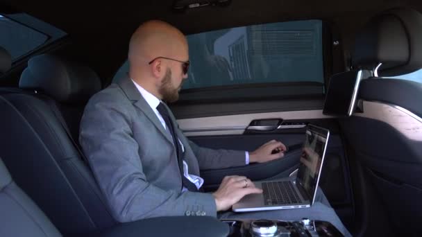 Schöner Geschäftsmann, der mit Laptop auf dem Rücksitz des Autos sitzt. Auto fahren und am Laptop arbeiten — Stockvideo