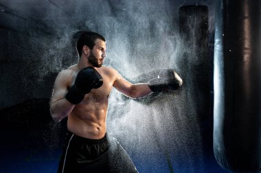 Erkek boksör boks stüdyosunda büyük bir kum torbasına vuruyor. Erkek boksör sıkı çalışıyor..