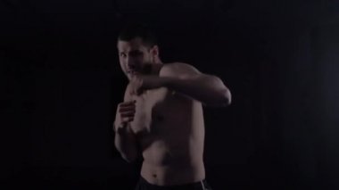 Erkek boksör kameraya yumruk atıyor. Siyah arka planda kameraya bakan boks antrenmanı yapan genç boksör silueti.