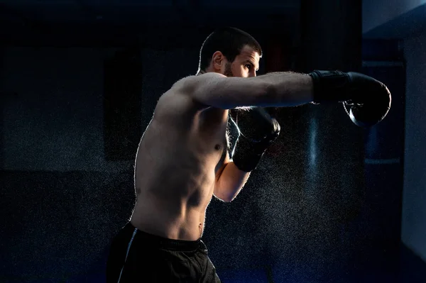 Młody samiec bokser uderzając worek bokserski na czarnym tle — Zdjęcie stockowe