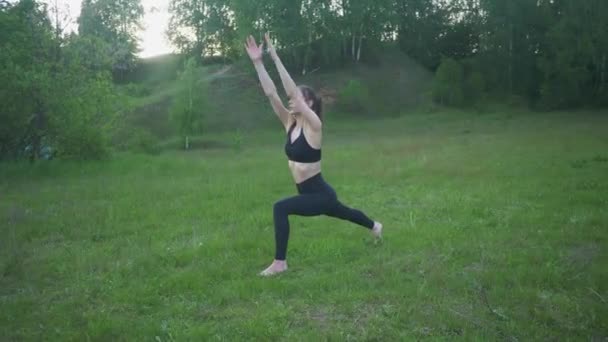 Jong atletisch meisje is bezig met yoga krijger pose outdoor — Stockvideo