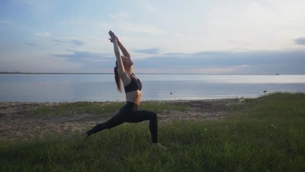 Jeune fille athlétique est engagé dans le yoga guerrier pose en plein air — Video