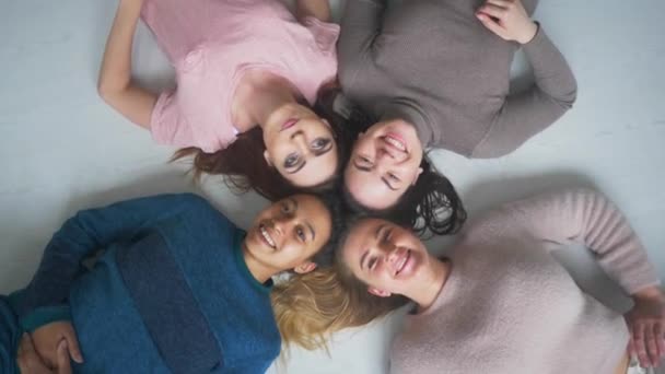 Cuatro feliz diversa etnia niñas bonitas mujeres amigas acostadas en círculo mirar a la cámara juntos, fiesta de pijamas y el concepto de amistad multiétnica, retrato de vista superior — Vídeos de Stock