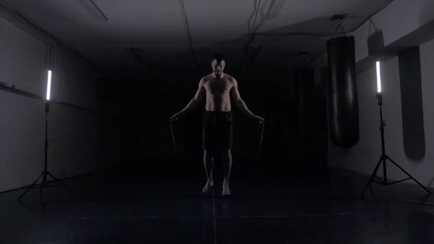 Boxer hace algunos ejercicios de cuerda de salto en el cuarto oscuro bajo la luz. Entrenamiento de combate en estudio ahumado en cámara lenta . — Vídeo de stock