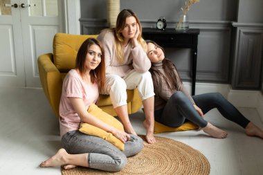 Üç çekici kız arkadaş kanepede oturuyor, heyecanlı bir şekilde konuşuyor, gülümsüyor.