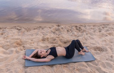 Kumsaldaki genç kız yoga minderinde yatıyor.