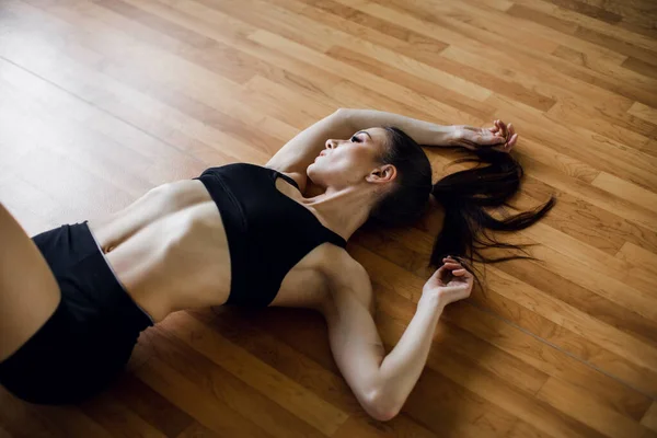 Mujer joven yace en el suelo después de su entrenamiento y mirando hacia abajo. Atleta femenina descansando después del entrenamiento físico — Foto de Stock