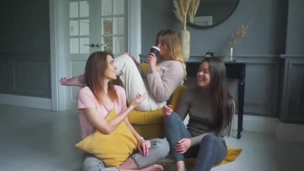 Три привлекательные девушки сидят на диване, взволнованно разговаривают, улыбаются — стоковое видео