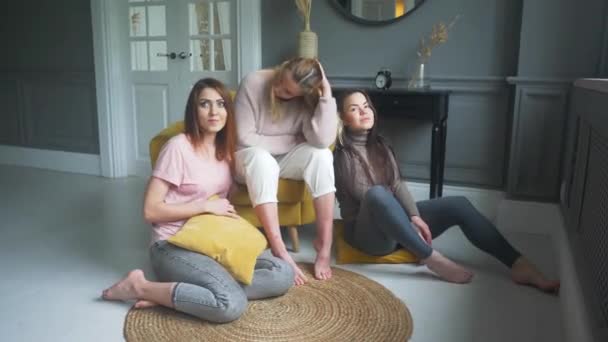 Три привлекательные девушки сидят на диване, взволнованно разговаривают, улыбаются — стоковое видео