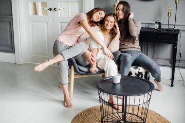 Üç çekici kız arkadaş kanepede oturuyor, heyecanlı bir şekilde konuşuyor, gülümsüyor.