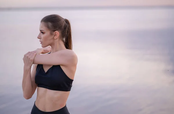 Chica joven en ropa de fitness junto al mar realiza ejercicios — Foto de Stock