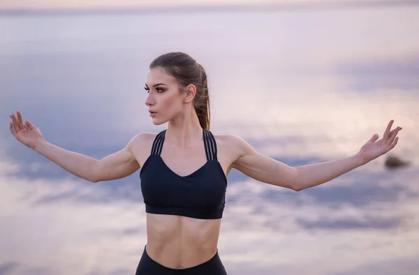 Ung vacker flicka värmer upp innan du gör yoga på stranden vid solnedgången — Stockfoto