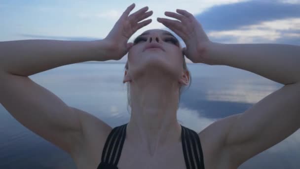 Молодая девушка растягивается на берегу моря на закате. тренировки на открытом воздухе или йога — стоковое видео