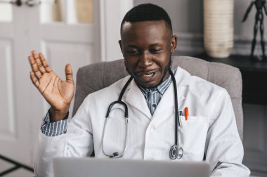 Siyah doktor bir hastayla iletişim kurmak için dizüstü bilgisayar kullanıyor. Gülümseyen erkek Afro-Amerikan profesyonel doktor.. 