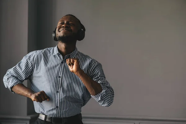 Guapo hombre de negocios afroamericano en ropa casual y auriculares está escuchando música usando un teléfono inteligente — Foto de Stock