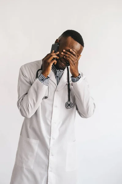Poważnie zdziwiony afro-amerykański lekarz rozmawiający przez telefon. Doktor otrzymał złe wieści oczekując pozytywnego wyniku. Białe tło — Zdjęcie stockowe