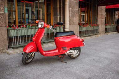 Şehrin boş caddesinin kaldırımına park edilmiş kırmızı renkli scooter.