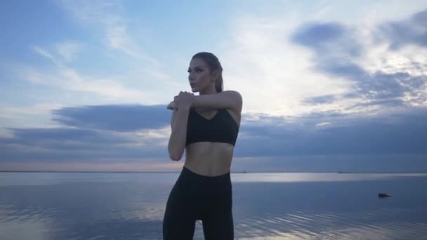 Un joven atleta hace un estiramiento en la playa. Chica atlética haciendo deportes al aire libre — Vídeos de Stock