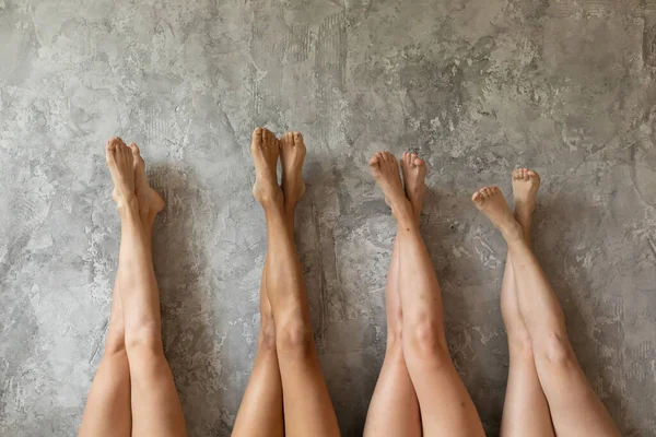 Four young women lying with legs up. Beautiful sexy multiethnic girls best friends lying in row raise legs up — Stock Photo, Image