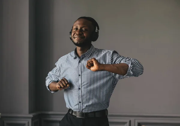 Hombre afroamericano en camisa elegante en auriculares escuchando música y disfrutando de la música, bailando — Foto de Stock