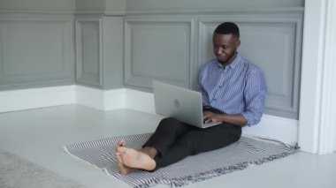 Genç bir Afro-Amerikalı öğrenci evde dizüstü bilgisayarda çalışıyor ve yerde oturuyor. iş ya da evde öğrenim