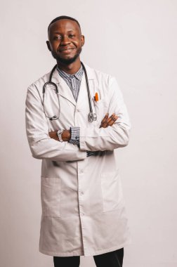 Siyah, genç, gülümseyen bir doktor beyaz arka planda duruyor.