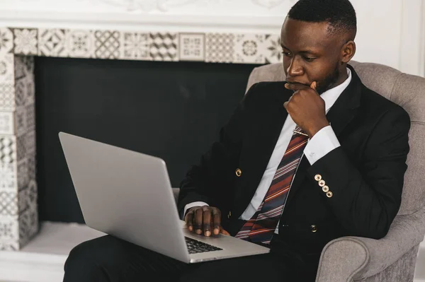 Homem de negócios preto sentado em uma cadeira em pensamento com um laptop em suas mãos — Fotografia de Stock