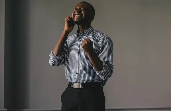 Negro chico en un gris fondo hablando por teléfono feliz aprende la buena noticia — Foto de Stock