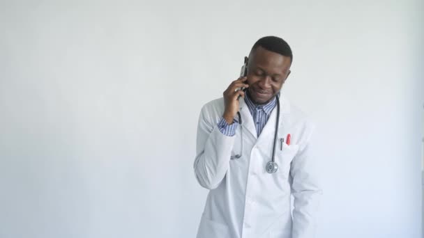 Černý-skinned mladý medik úsměv stojící na bílém pozadí mluvit do telefonu — Stock video