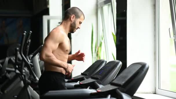 En man med naken överkropp springer på ett löpband. hälsosam livsstil. uppvärmning före träning — Stockvideo