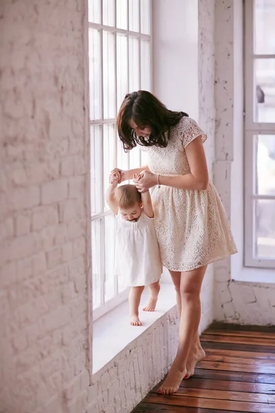 Una joven madre le enseña a caminar a su pequeña hija. Bebé primer paso —  Fotos de Stock