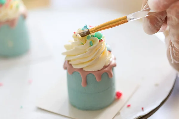 making cupcake confectioner decorates sweets with a brush