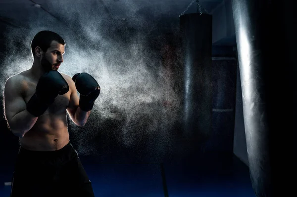 Thai boxing fighter on a dark background hits a boxing bag. Advertising Martial Arts Fitness Center