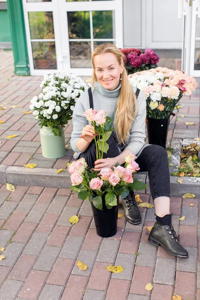 Жіночий флорист сидить біля входу в магазин, оточений квітами. Ділова жінка — стокове фото