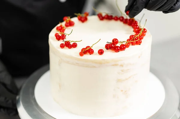 Μια επαγγελματίας σεφ ζαχαροπλαστικής ετοιμάζει ένα γλυκό κέικ στην κουζίνα, βάζοντας κόκκινα φραγκοστάφυλα σε αυτό — Φωτογραφία Αρχείου