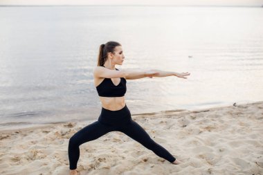  Kumsalda sabah egzersizi yapan güzel bir kadın. Deniz kenarında yoga meditasyonu. Güzel gün doğumu. Yoga pozları