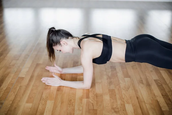 Ganzheitliche Seitenansicht einer jungen schönen Frau in Sportbekleidung, die ein Board macht, während sie vor einem Fenster in der Turnhalle steht — Stockfoto