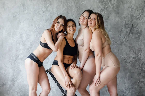 Vriendschap, schoonheid, lichaam positief en mensen concept - groep van gelukkige vrouwen verschillend in ondergoed over grijze achtergrond — Stockfoto