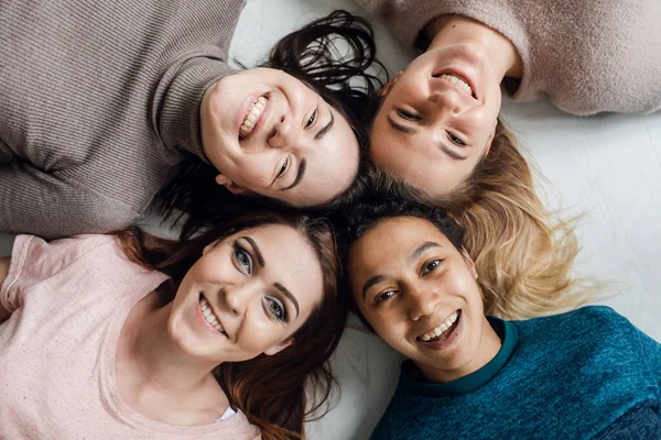 Quatro felizes etnia diversa meninas bonitas mulheres amigas deitadas em círculo olham para a câmera juntas, festa do pijama e conceito de amizade multiétnica, retrato de vista superior — Fotografia de Stock