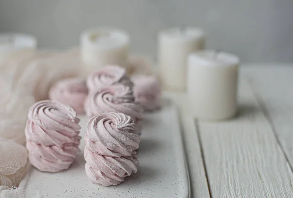 Hausgemachter Eibisch-Zephyr mit Kerzen auf einem weißen Teller auf einem hellen Holztisch. rosa süßer, hausgemachter Eibisch oder Eibisch. bunte Baiser auf weißem Hintergrund. Dessert — Stockfoto